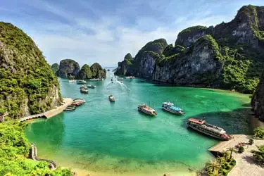 Emerald waters of Ha Long Bay in Vietnam, with limestone karst islands, traditional cruise boats, and lush greenery surrounding a calm tropical lagoon.