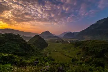 Sunrise over the Mai Chau Valley in northern Vietnam, with misty mountains, rolling green rice fields, and layered hills glowing in soft golden morning light.