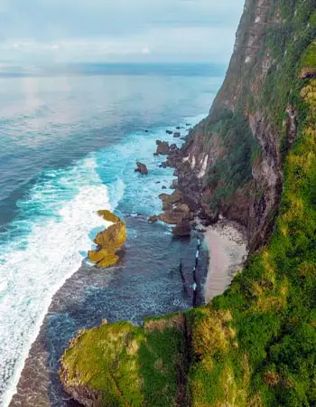 Dramatic cliffside coastline in West Bali, Indonesia, featuring rugged limestone cliffs and crashing waves along a secluded stretch of shoreline.