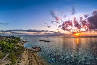 Sunset over the coastline of Sanur Beach with calm ocean waters and tranquil shoreline.