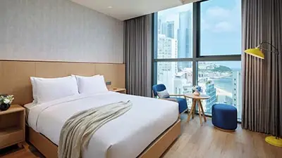 Bright modern guest room at L7 Haeundae by Lotte in Busan, South Korea, featuring floor-to-ceiling windows with ocean and city views near Haeundae Beach.