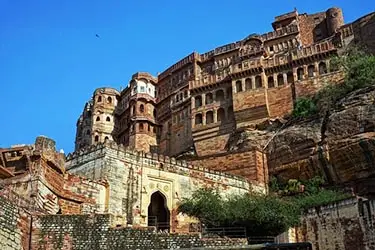 Mehrangarh Fort in Jodhpur, India, rising dramatically above the city on a rocky hill, with massive stone walls, intricate facades, and a grand प्रवेश gate.