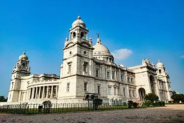 Victoria Memorial in Kolkata, India, a grand white marble building with domes and classical columns, set against a clear blue sky.