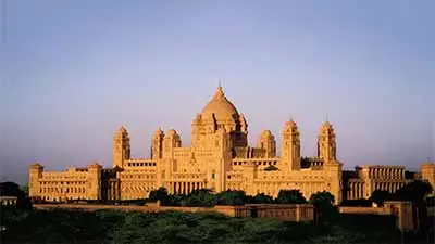 Umaid Bhawan Palace in Jodhpur, India, a grand sandstone palace with a central dome and expansive wings, glowing in warm evening light.