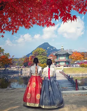 Two women in traditional Korean hanbok walking through Gyeongbokgung Palace during autumn in Seoul.