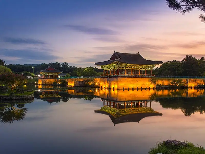 Donggung Palace and Wolji Pond in Gyeongju at sunset, with illuminated traditional pavilion reflected in calm water, showcasing historic Silla-era architecture in South Korea.