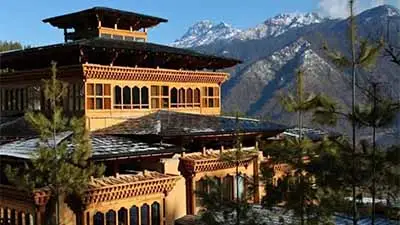Naksel Boutique Resort in Paro, Bhutan, featuring traditional Bhutanese architecture set among pine forests with snow-capped Himalayan mountains in the background.