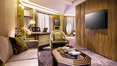 Elegant guest suite at The Landis Taipei featuring warm wood interiors, lounge seating area, work desk, and modern amenities.