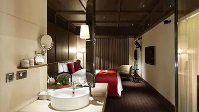 Luxury guest room at Palais de Chine Hotel Taipei featuring an open-plan bathroom with soaking tub, dark wood interiors, and elegant modern furnishings.