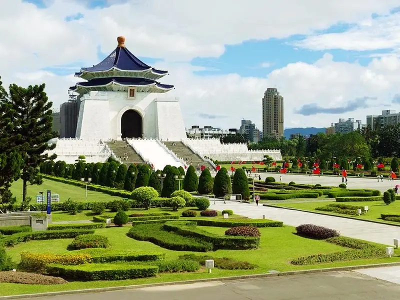 Iconic Chiang Kai-shek Memorial Hall surrounded by manicured gardens and pathways, featuring its white marble structure and blue-tiled roof set against the Taipei skyline.