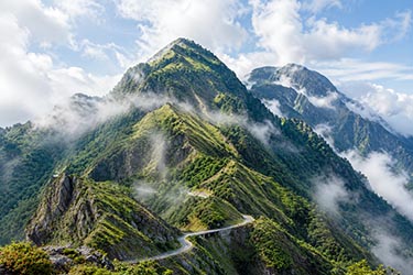 Mist-covered mountain peaks along Taiwan’s Hehuanshan mountain road, with winding alpine roads cutting through lush green ridges beneath low clouds.