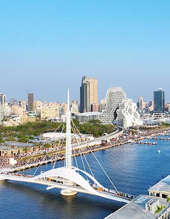 Scenic view of Kaohsiung Harbor in Taiwan featuring the Great Harbor Bridge, modern waterfront architecture, and the iconic Kaohsiung Music Center along the city's vibrant skyline.