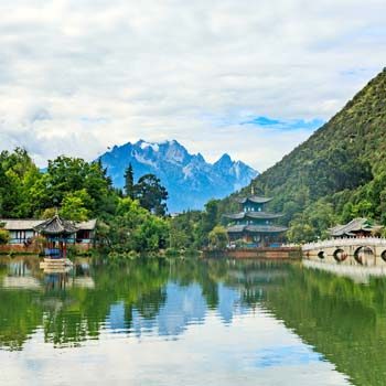 Black Dragon Pool (Heilongtan) in Lijiang, Yunnan, with traditional pavilions, arched stone bridges, and Jade Dragon Snow Mountain reflected in the calm water.