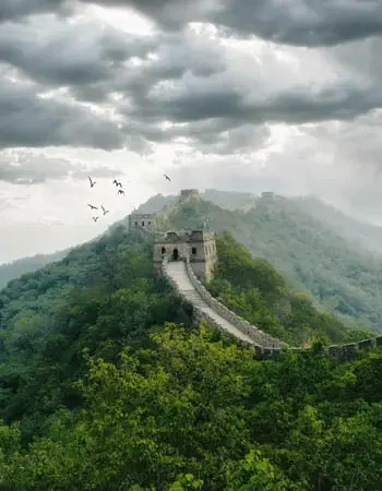 China_350-450_Great-Wall Great Wall of China stretching across misty green hills under dramatic skies, highlighting one of the country’s most iconic landmarks.
